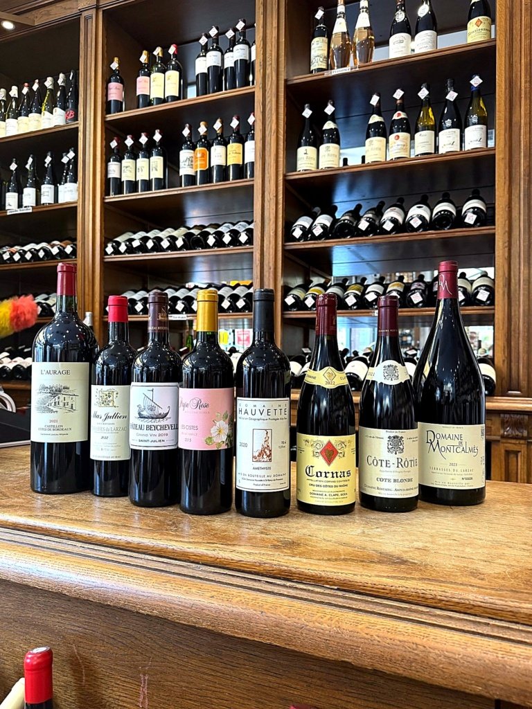 Vins rouges alignés sur le comptoir du caviste Maison Busquets à Toulouse, devant les rayonnages de la cave
